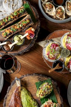A spread of tapas and small plates on wooden boards: sandwiches, tacos, deviled eggs, grilled veggies, dips, and colorful small bites, all inviting.
