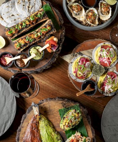 A spread of tapas and small plates on wooden boards: sandwiches, tacos, deviled eggs, grilled veggies, dips, and colorful small bites, all inviting.