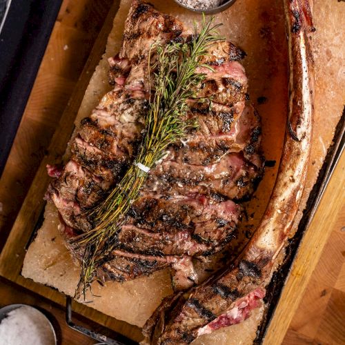 Grilled rack of lamb with a rosemary sprig, three dipping bowls, and a bone-in chop on a wooden serving board, ready to eat.